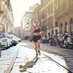Energetic woman jogger running down a city street in active wear on a sunny day.